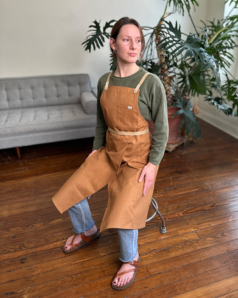 Person wearing a split-leg copper ceramics apron in a studio beside plants. 